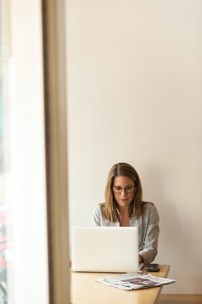 身穿灰色条纹连衣裙衬衫的女子坐在白色笔记本电脑前棕色木桌旁